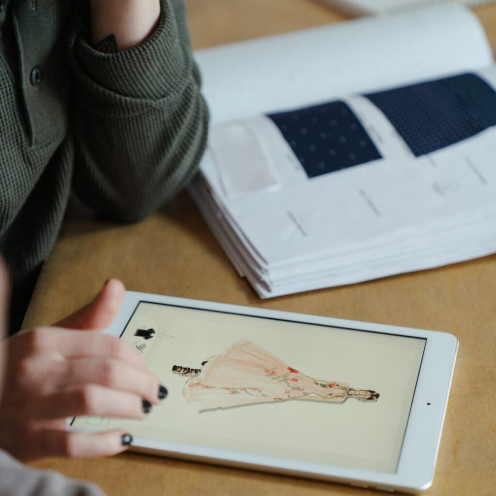 Person in gray sweater holding a white tablet designing a dress
