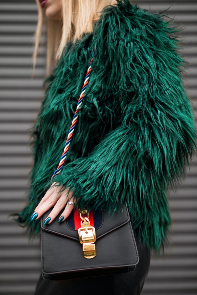 Photo of a woman wearing a green fur coat holding a black purse