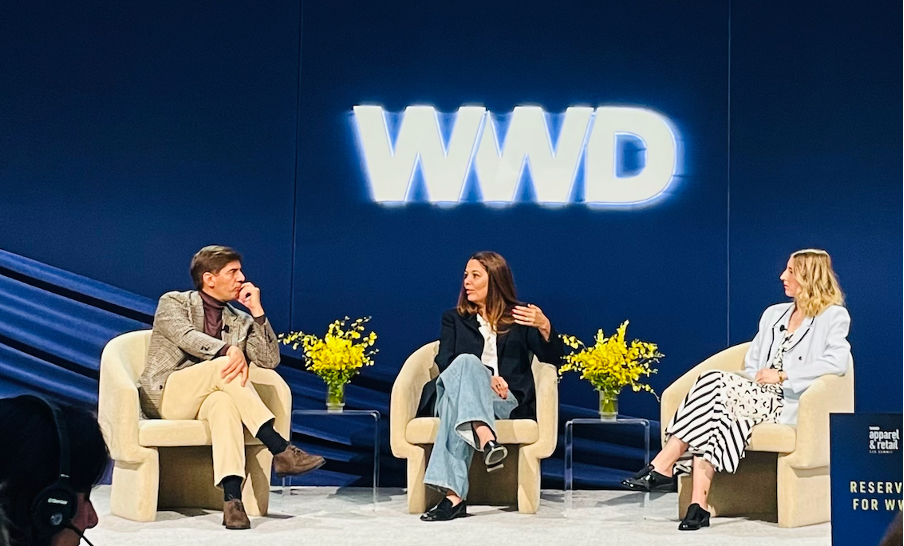 Photo of three people seated on stage with the WWD logo above them