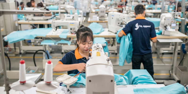 Workers in a Tal Apparel factory assembling an order, wearing blue shirts with orange collars.