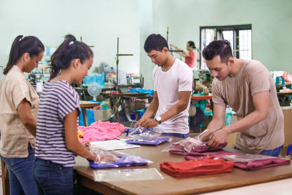 Two women and two men work at a packaging table in a textile factory