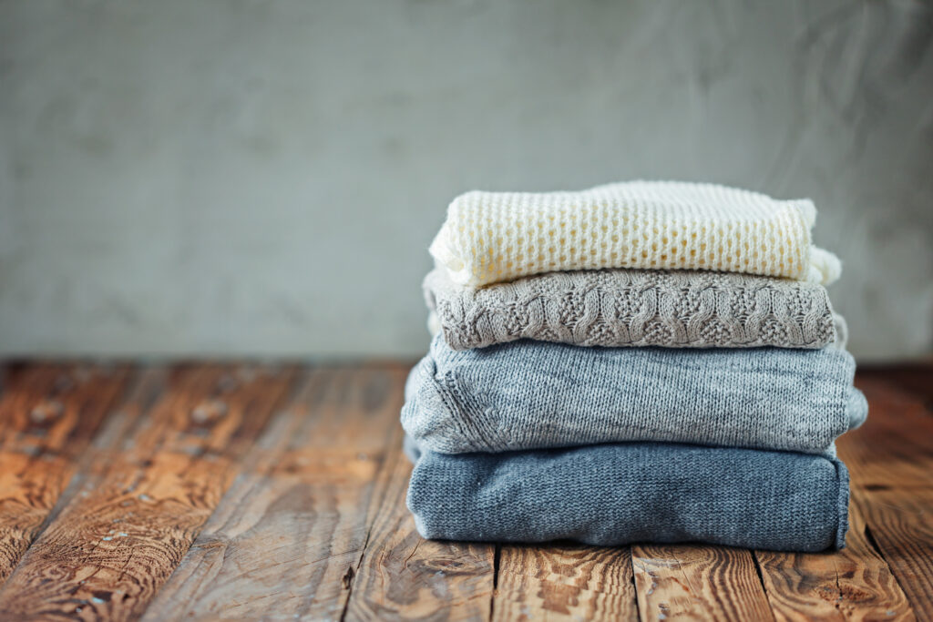 Stack of knitted winter sweaters on wooden background