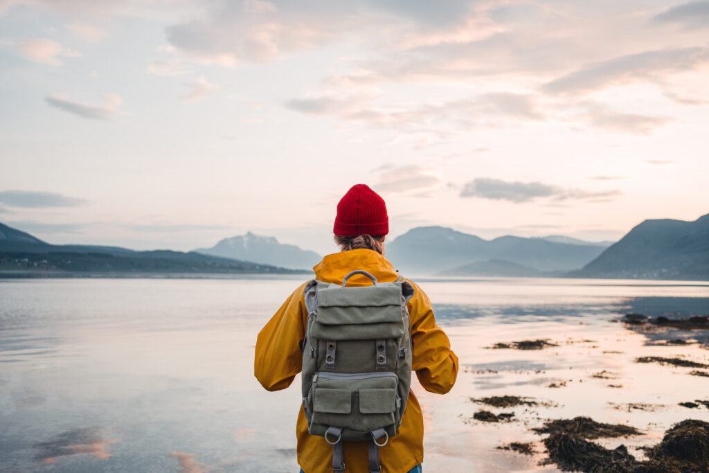 Back view of male with rucksack standing on coast in front of mountains