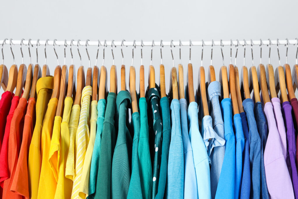 Rack with bright clothes on light background. Rainbow colors