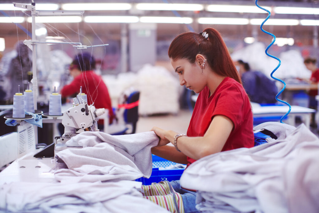 Higg FEM 2025 update unlocks new data-driven insights for manufacturers. Here, a factory in full motion with a female worker in red sewing.