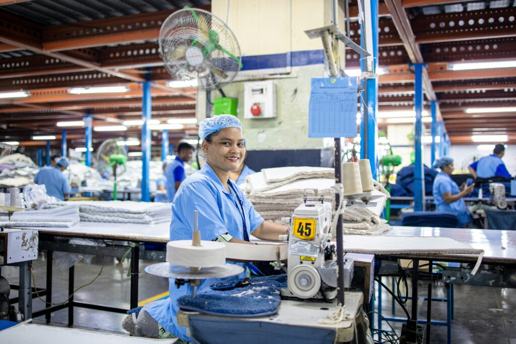 A garment worker in a factory smiles while working on textiles. Image courtesy of EqualStock via Unsplash