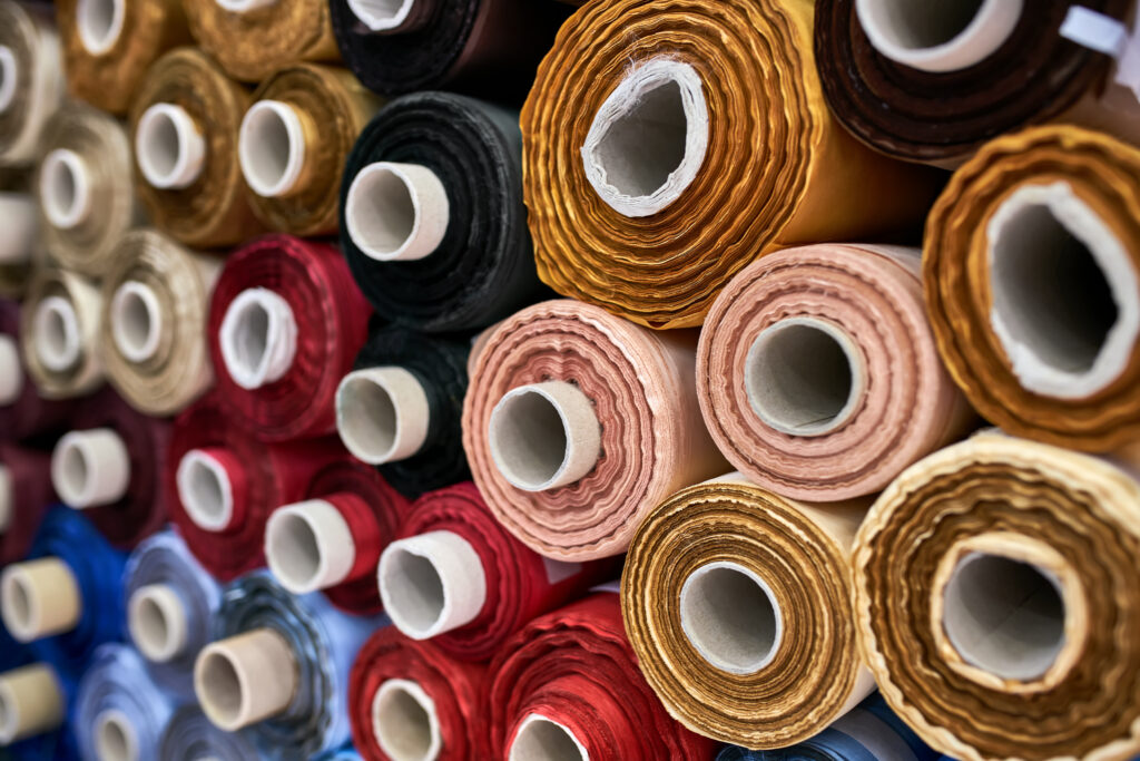 Wonderful multicolored fabric rolls are lying on each other inside a warehouse. Closeup horizontal photo with selective focus.