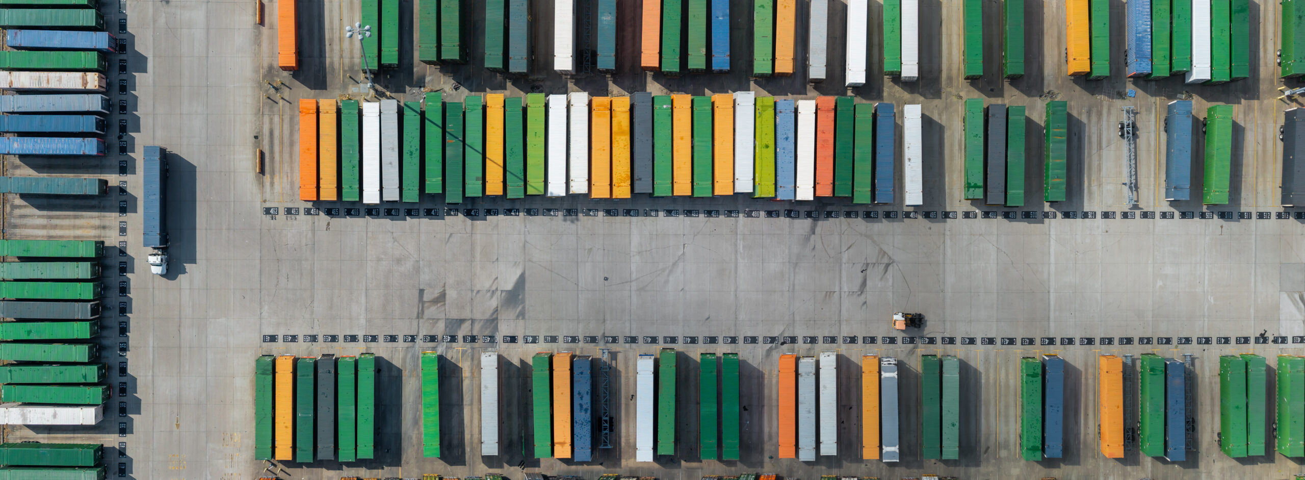 Freight containers stacked in an industrial yard with a truck and forklift moving cargo in Texas.
