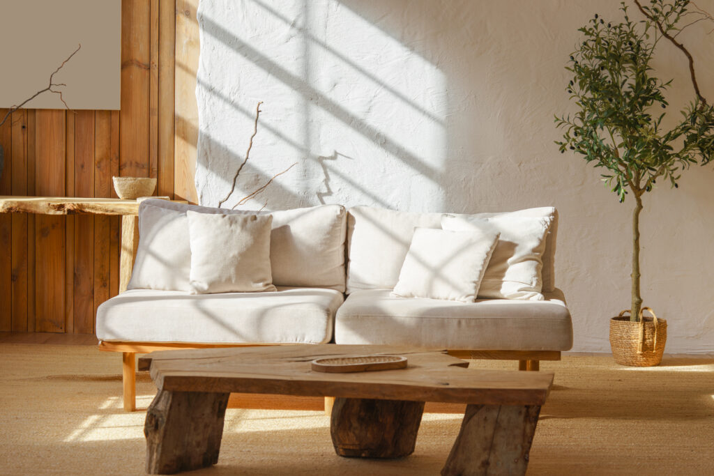 Bright cozy living room with light beige sofa, rustic wooden coffee table and sunlight streaming through window. Home interior design in scandinavian style with warm tones and natural materials.