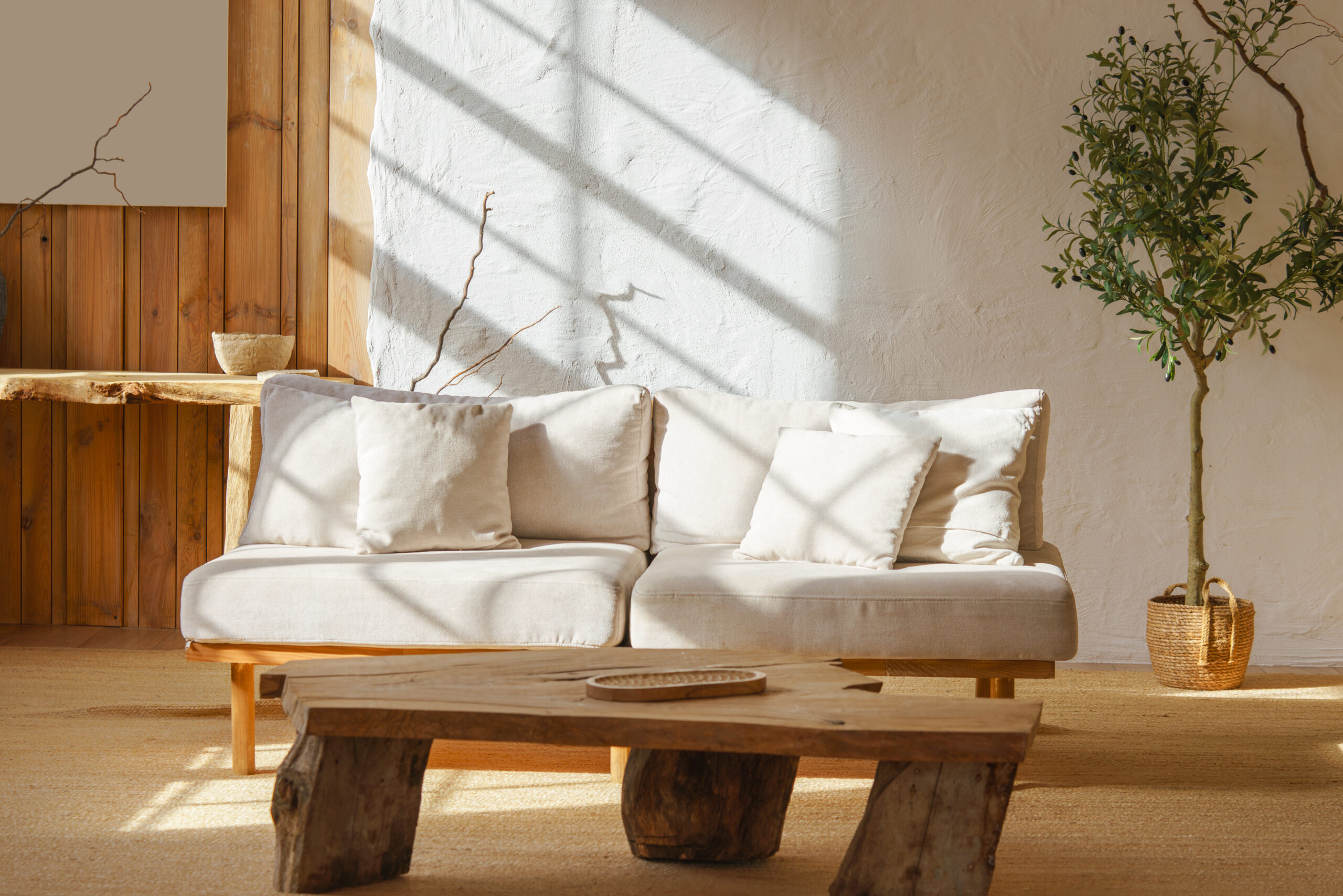 Bright cozy living room with light beige sofa, rustic wooden coffee table and sunlight streaming through window. Home interior design in scandinavian style with warm tones and natural materials.