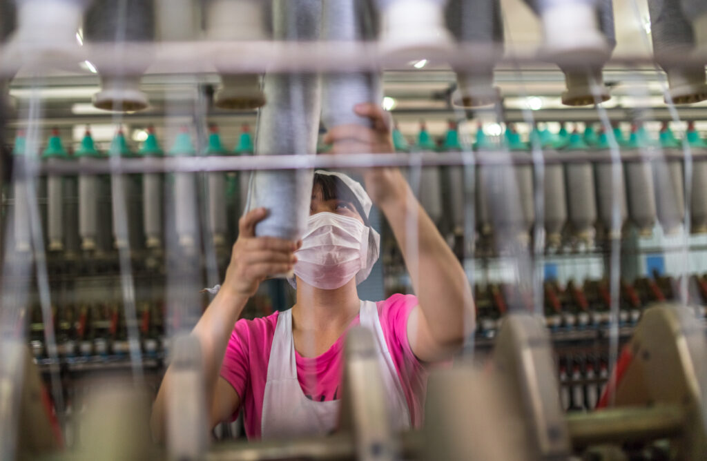 female worker standing beside thread making machine inside cotton mill,industry concepts.